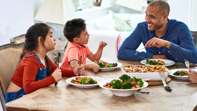 Cheerful father smiling and talking with family at meal time 